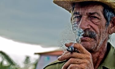 An old wearing a hat, smoking.