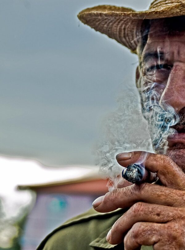An old wearing a hat, smoking.