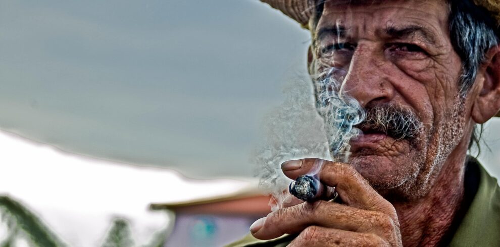 An old wearing a hat, smoking.