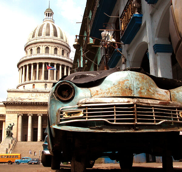 A car and behind is a historic building in Havana.