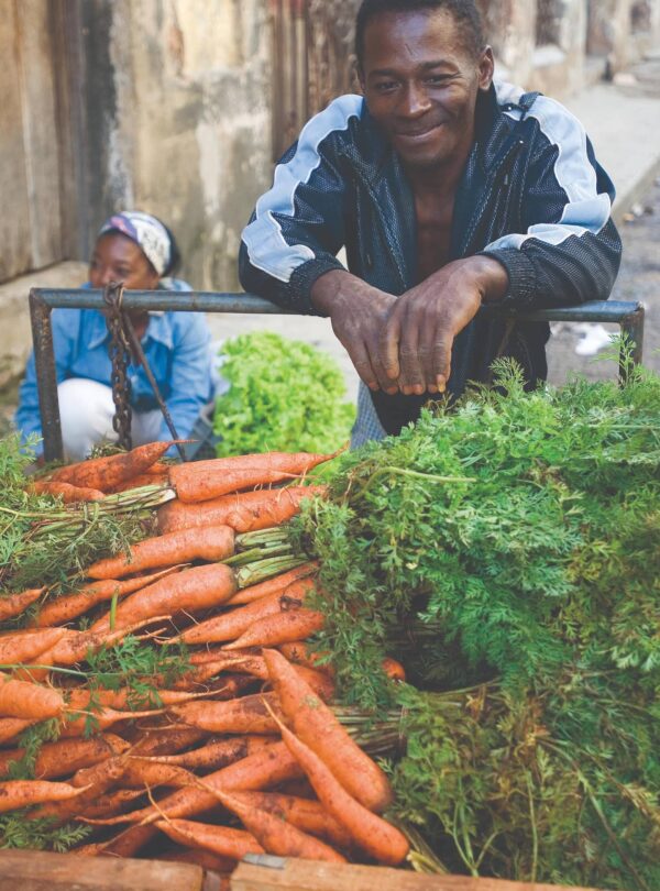 A smiling man selling carrots on the streets.